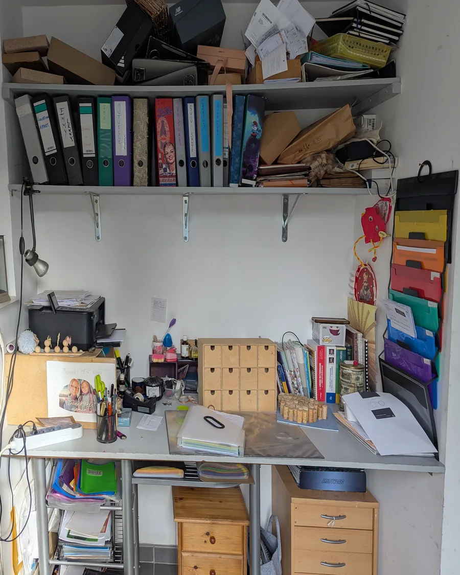 Coin bureau avant rangement : boîtes et papiers empilés sur l'étagère, plan de travail couvert d'objets