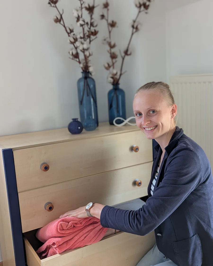 Coralie Poncelet range une serviette dans le tiroir d'une commode en bois clair